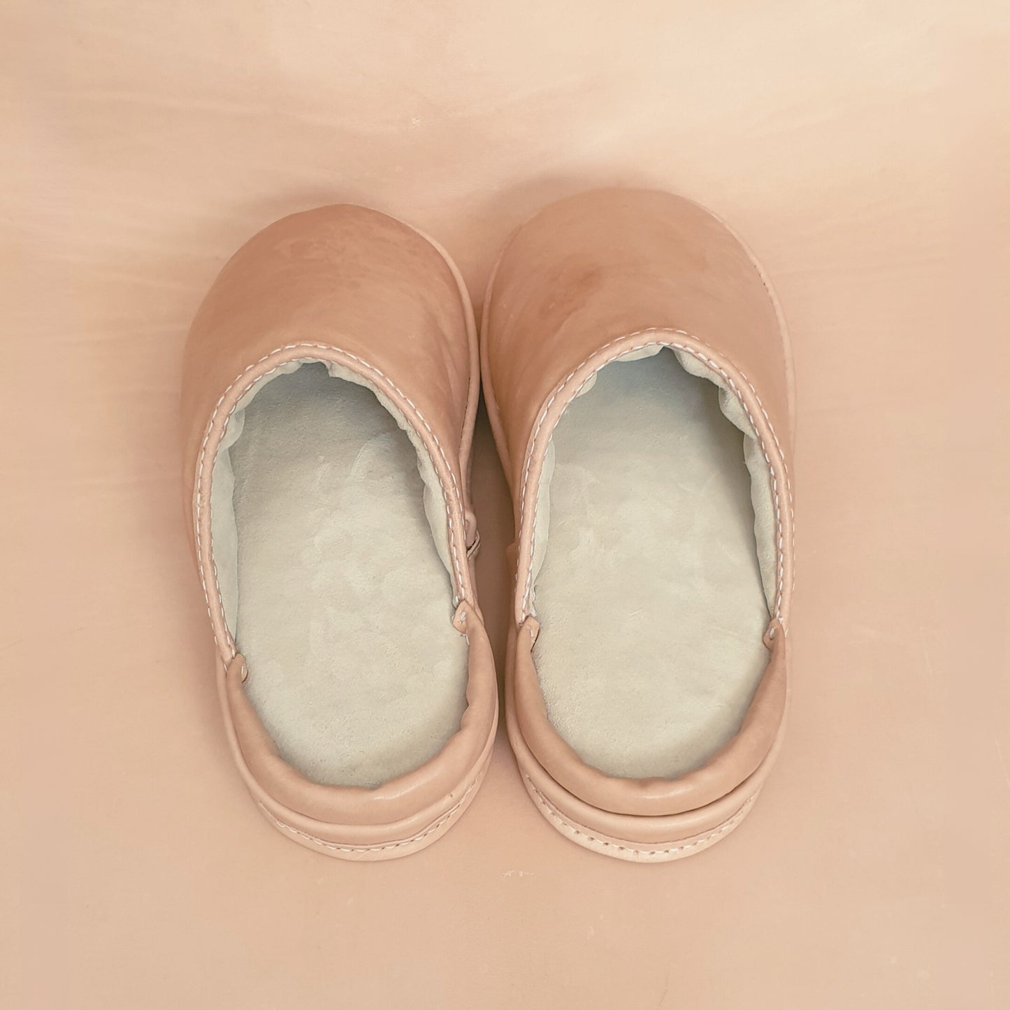 Pair of beige adaptive slippers on a matching background