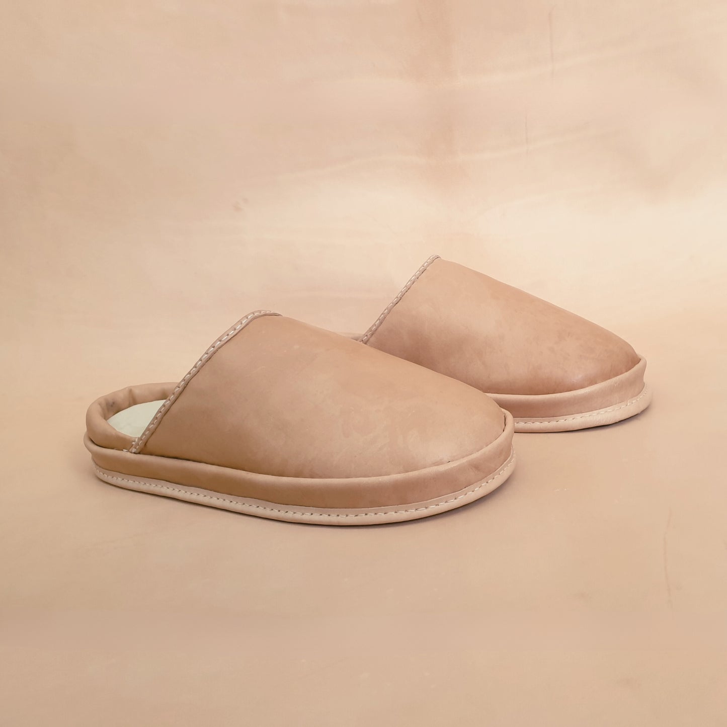 Pair of beige leather slippers on a beige background