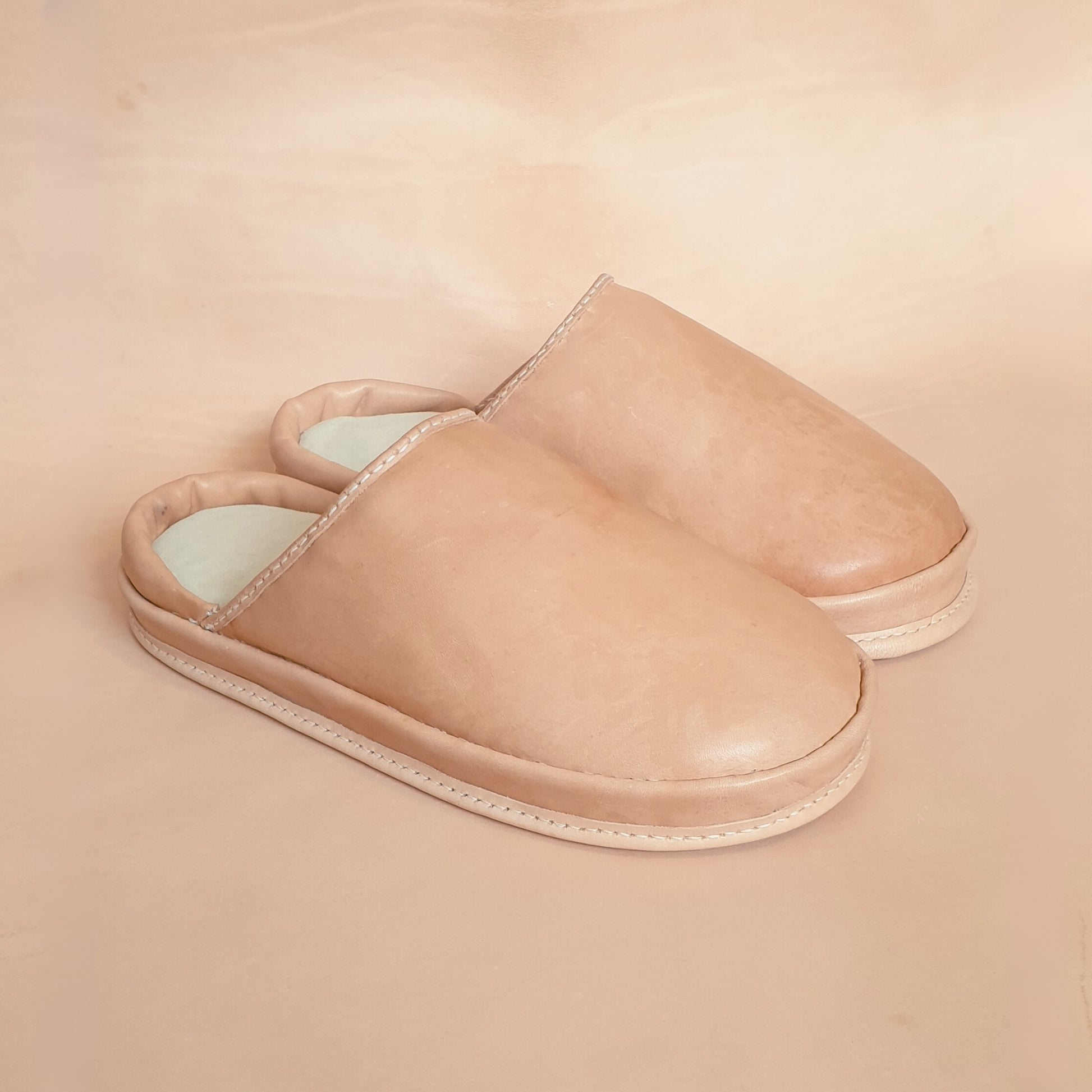 Pair of beige SPA GAIT leather slippers on a beige background