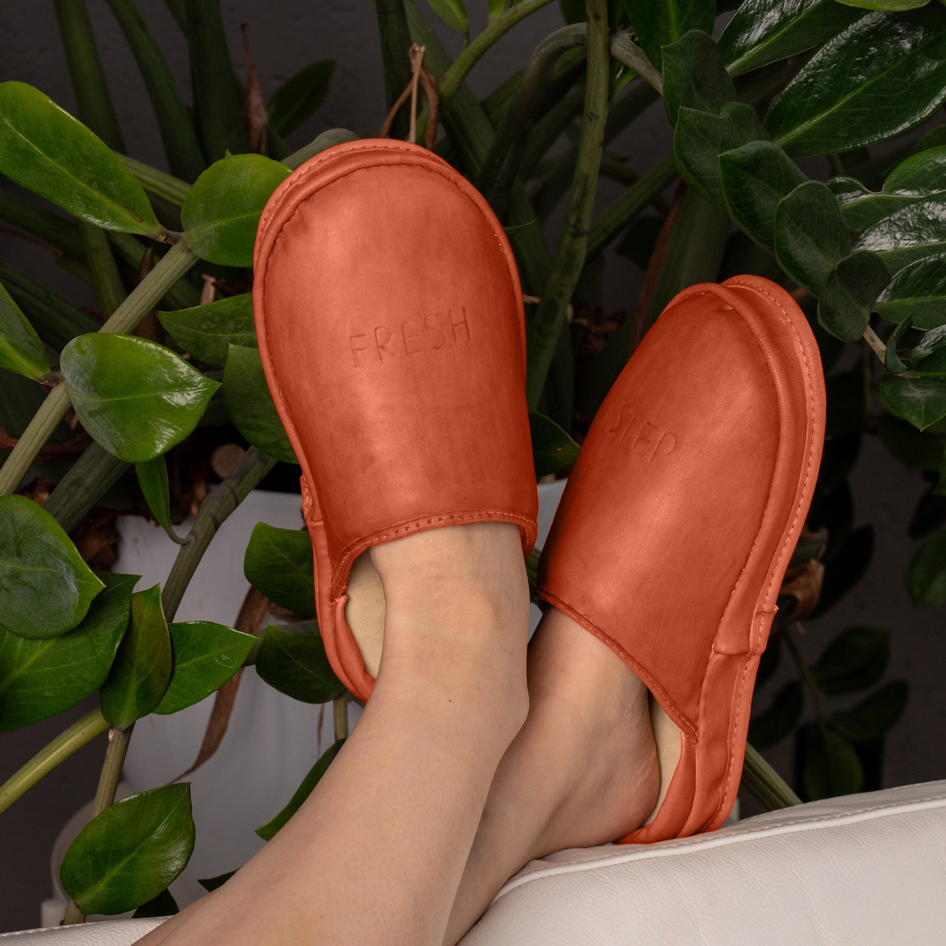 Clay Flame slip on leather clogs on a sofa. These soft slippers provide exceptional comfort for a relaxing lounge at home.